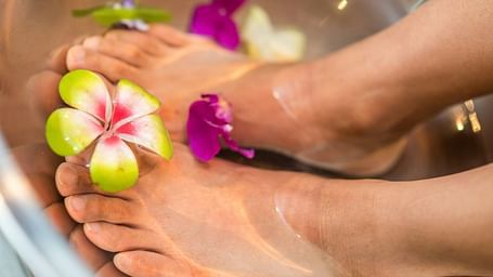 Feet soaking in water, adorned with colourful flowers.