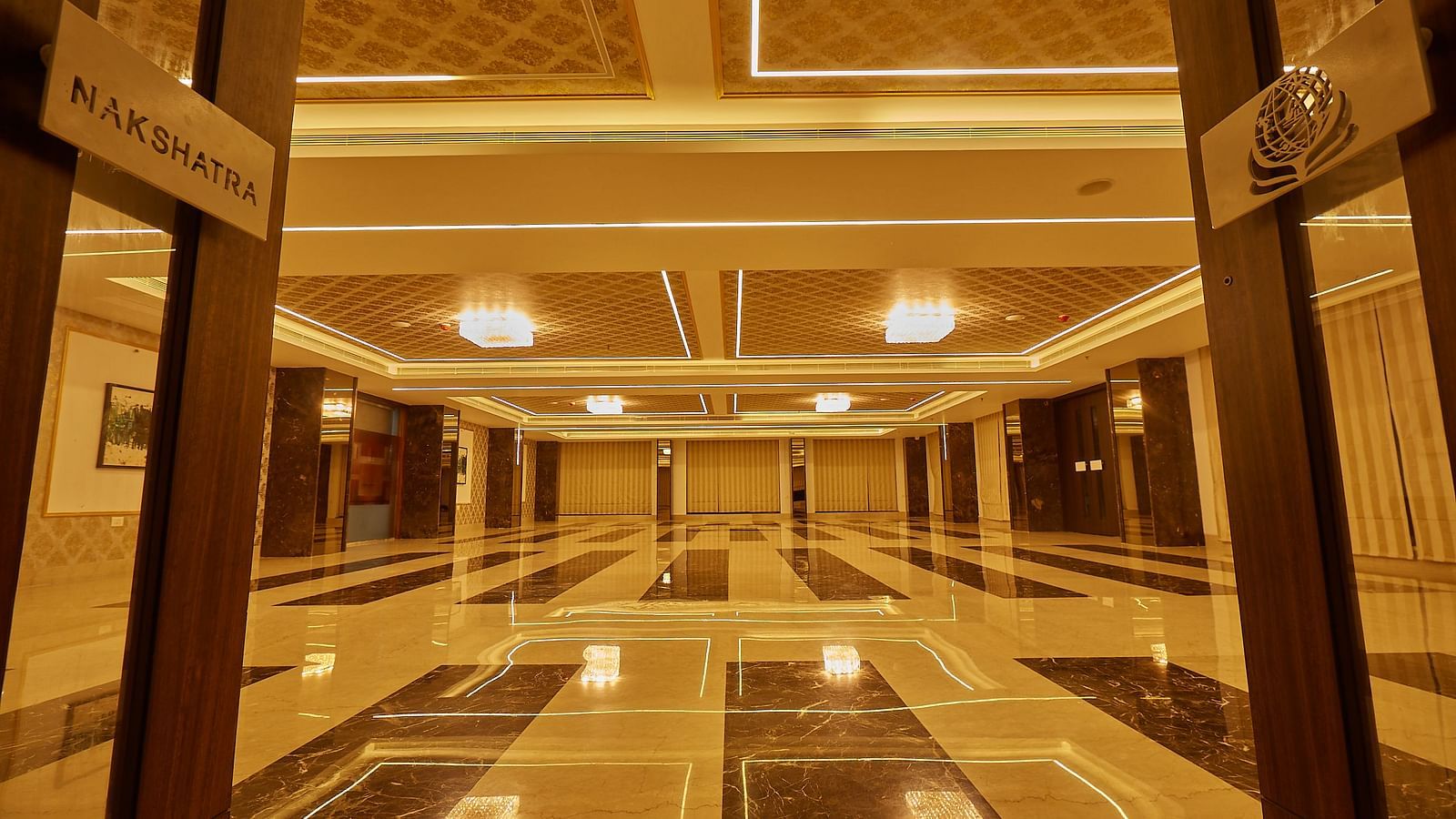 A long perspective of an empty, well-lit banquet hall with glossy, patterned floor tiles and decorative ceiling details.