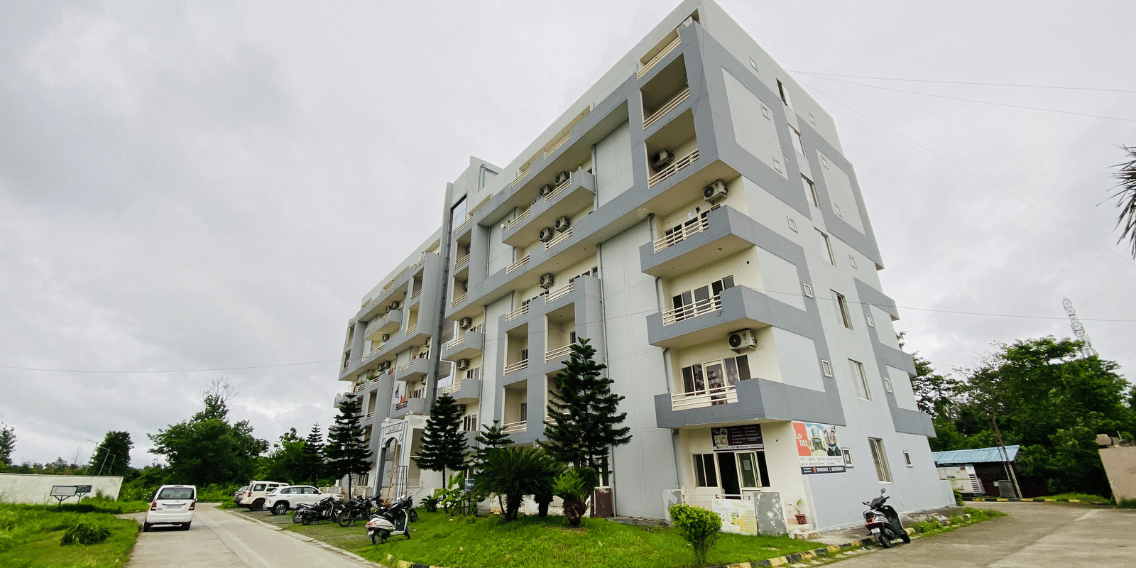 An exterior shot of a modern, multi-story white building with balconies and angular architecture under a cloudy sky.
