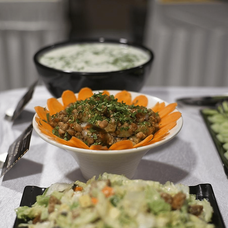 Two bowls of salad, one white and one orange, on a table with a blurred background.