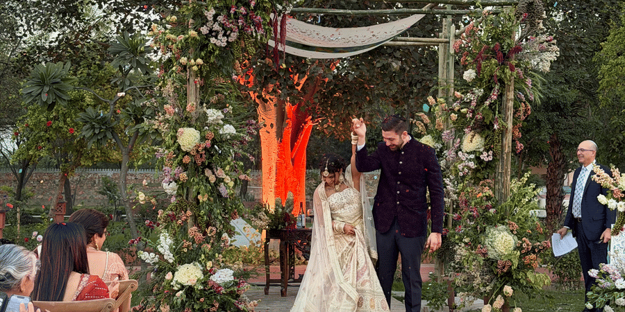 A bride and groom stand beneath a rustic floral structure at the end of a decorated garden pathway at Umaid Palace.