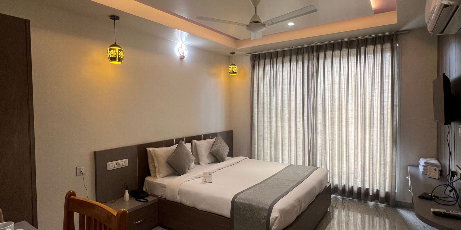 Wide view of the Daksh Comfort Room at Daksh The Valley Resort, Saputara, showcasing its centrally placed king size bed, closed curtains, warm overhead lighting, and marble flooring.