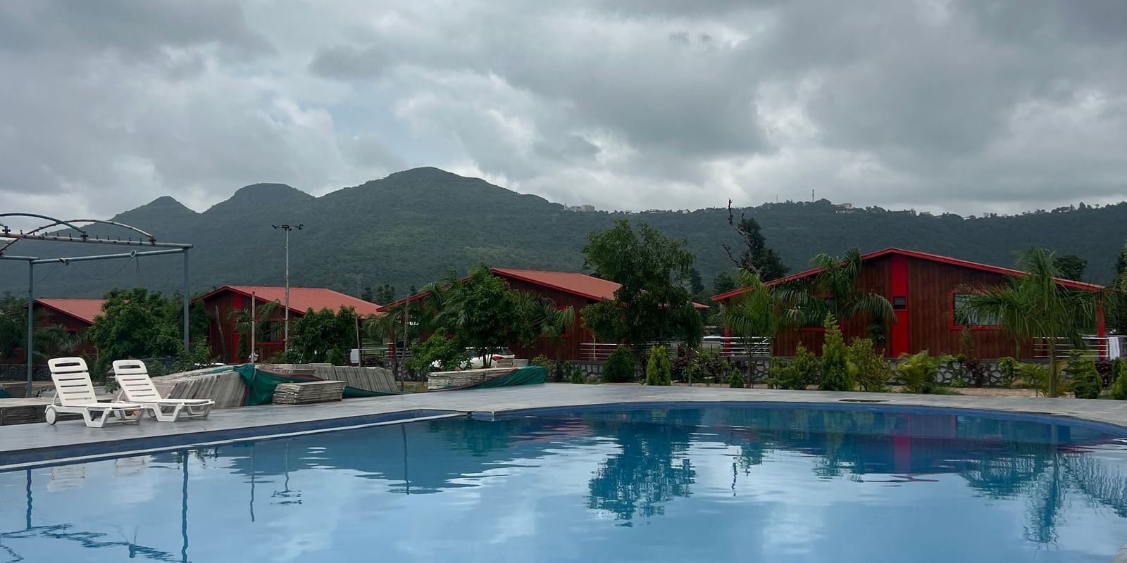 Panoramic scene of the resort swimming pool at Daksh The Valley Resort, Saputara, with water in the pool reflecting the sky and landscape.