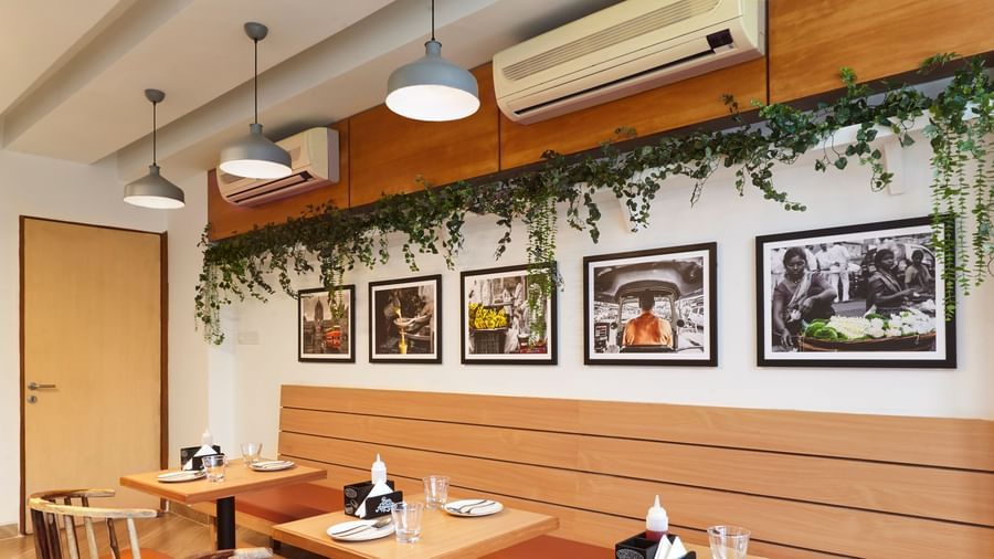 A section of the casual dining restaurant at Monday Hotels Mahape, Navi Mumbai, with wooden tables and chairs.