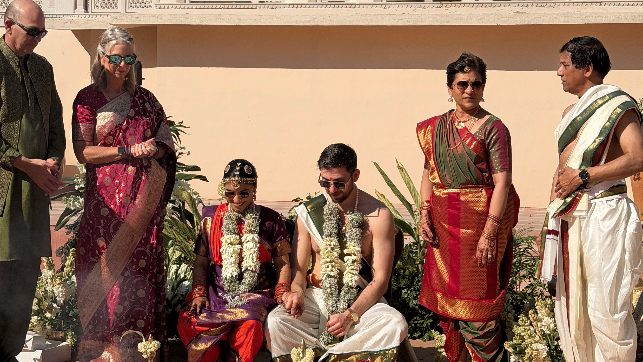 A family gathered together outdoors in a courtyard at Umaid Palace performing traditional Hindu wedding ceremony rituals on the ground.