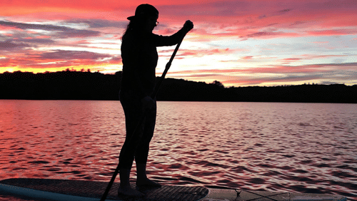 A person standing in shallow water during sunset with the sky in multi colour shades.