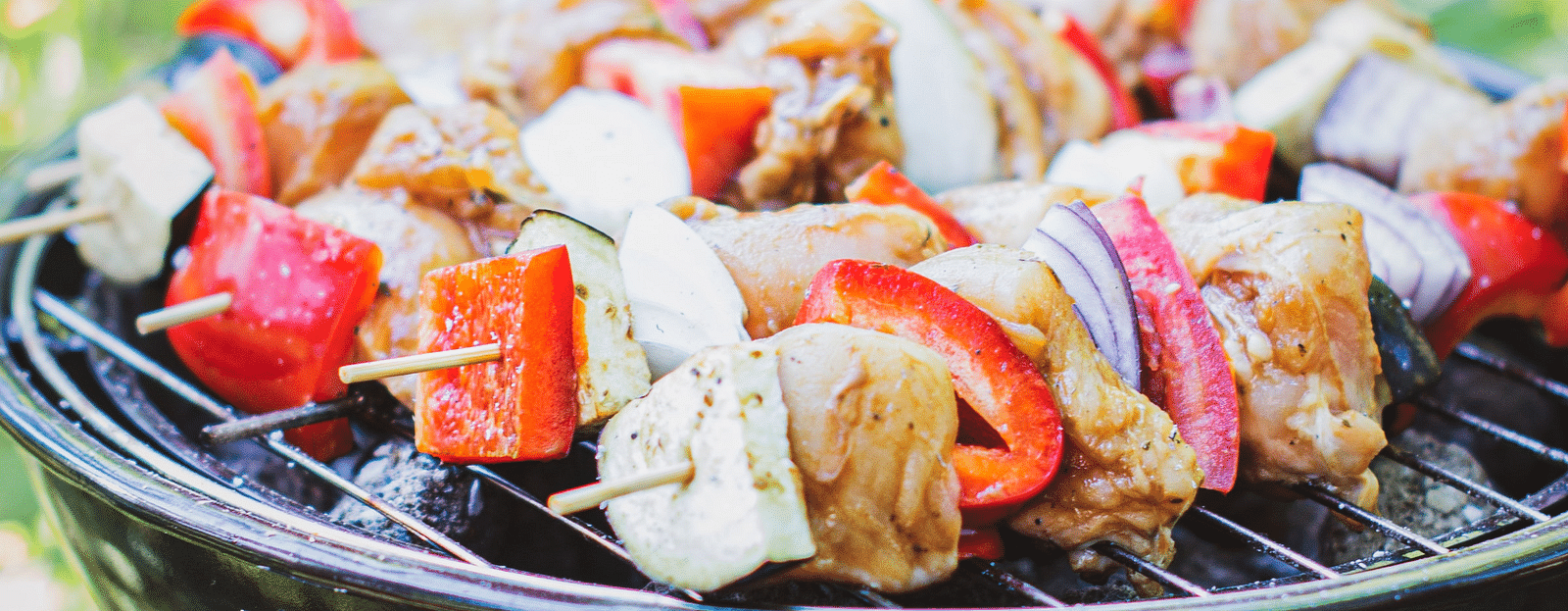 A barbecue grill set up in an open space, featuring skewers of vegetables and meat cooking over the flames