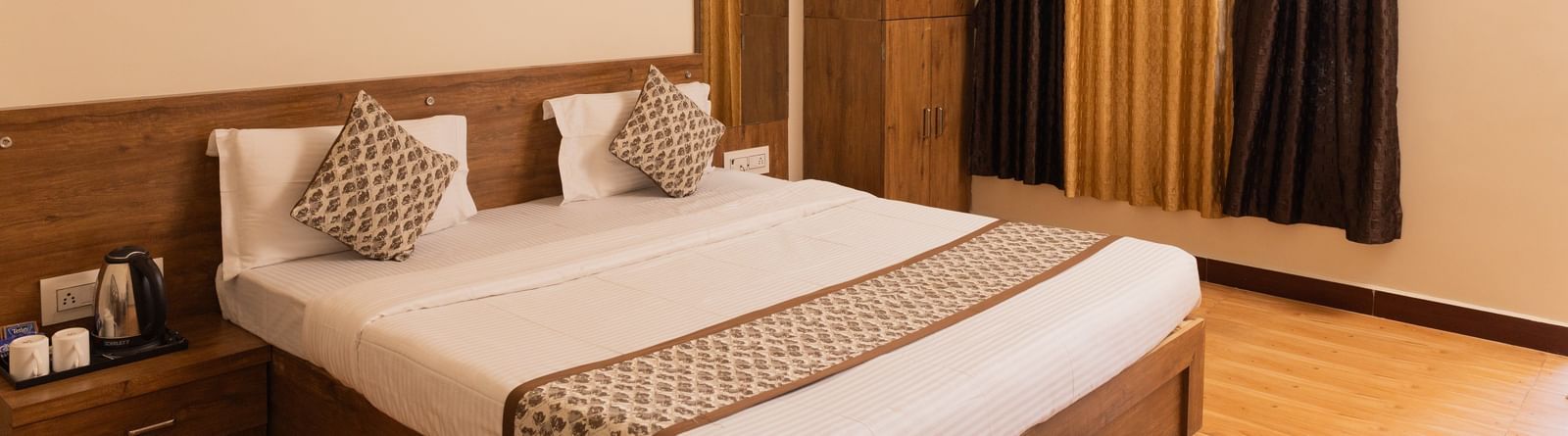 A neatly arranged double bed with patterned cushions and curtains at Daksh Resort & Amusement Park.