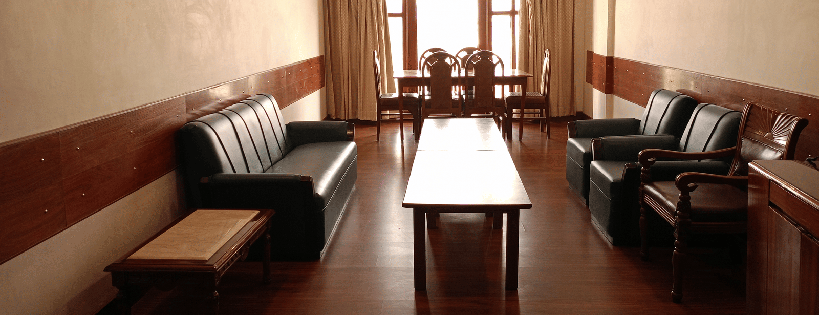 Sitting area at Hotel Gold, Panipat with sofas, a center table, and a large window at the far end.