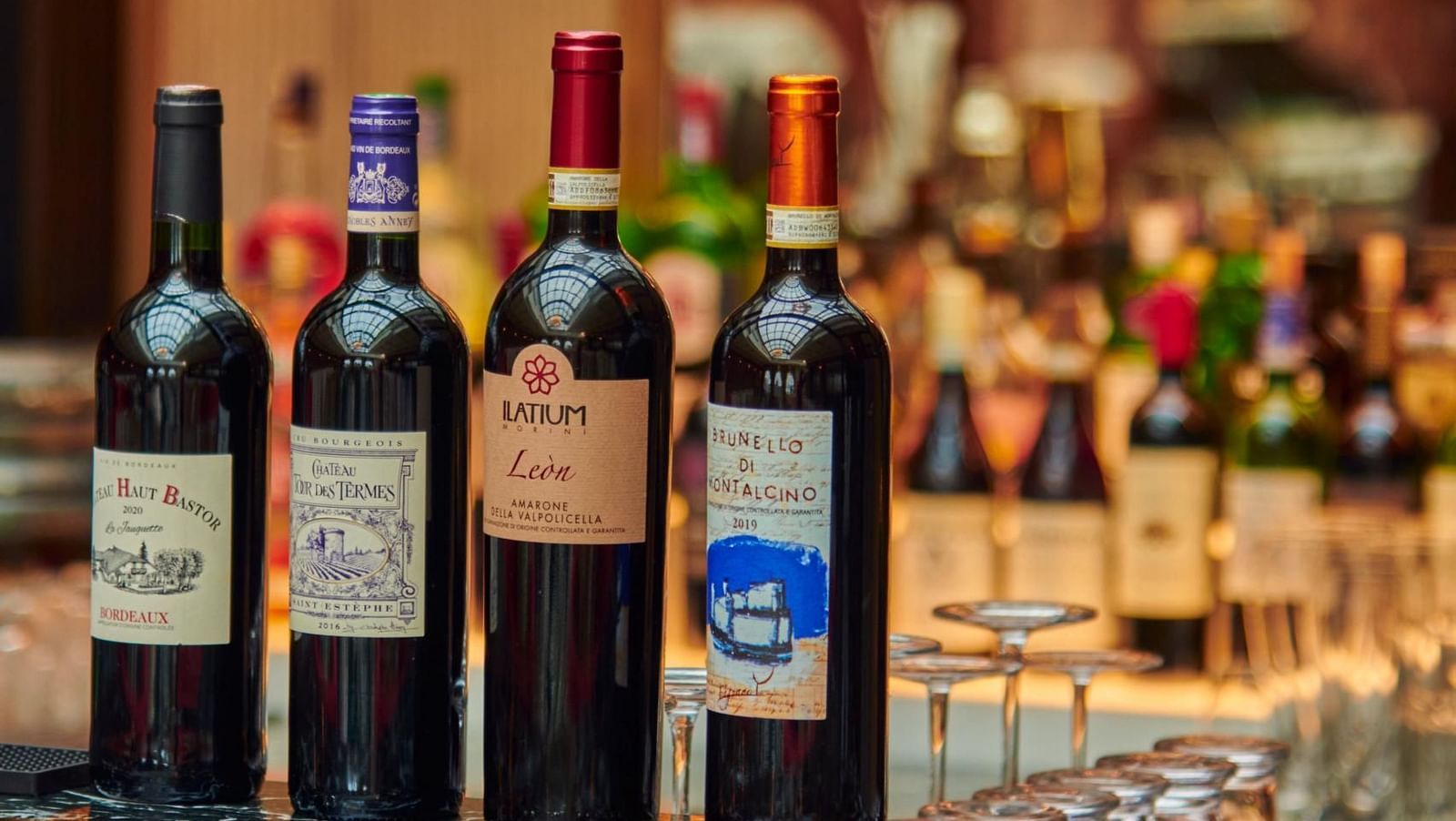 A row of wine bottles is displayed on a glossy bar counter, with shelves of various liquor bottles blurred in the background