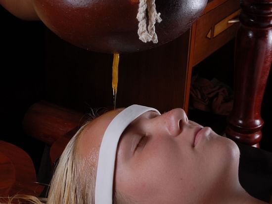 A person lying on their back with closed eyes receiving shirodhara therapy at UDS Group of Hotels