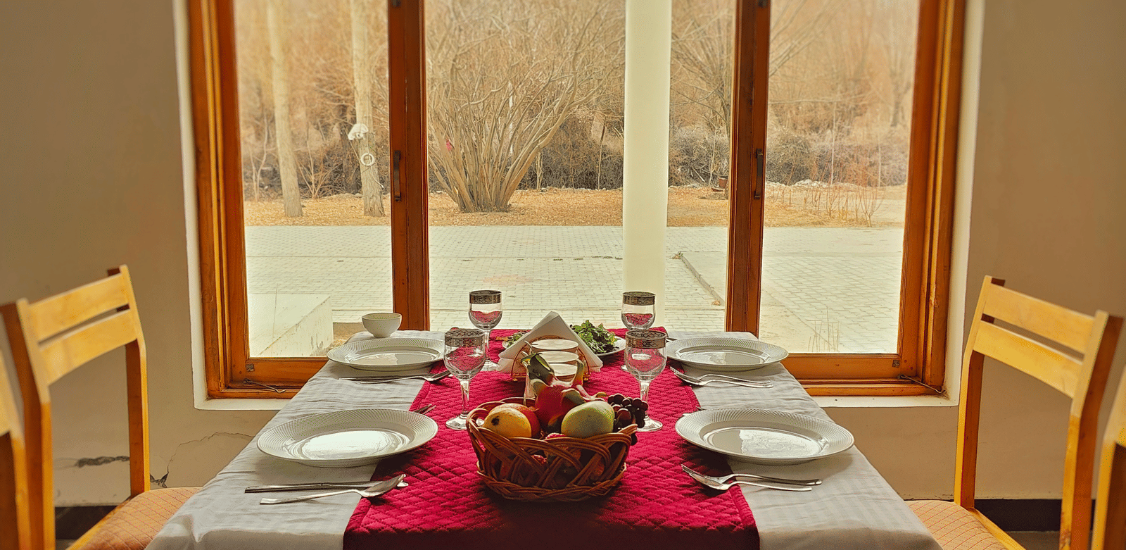 A wooden dining table for four set neatly in front of a large window with a scenic view at Indus Serenity Retreat.