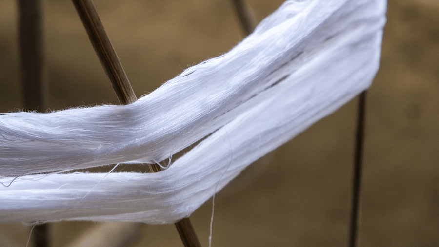 A vertical portrait detailing white cotton fibers on a primitive, rustic wooden spinning wheel.
