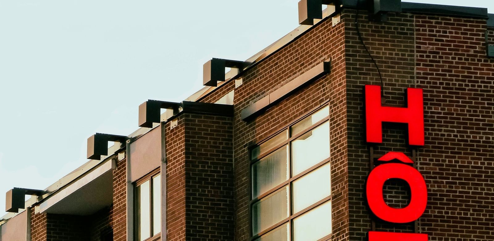 Close-up of the upper floors of an older, dark brick building with a vertical, bright red neon sign spelling out the word 'HOTEL'.