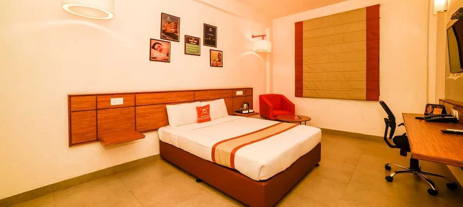 a spacious room with a queen size bed placed in the middle with small photo frames hung on the wall - Max Hotel Jabalpur
