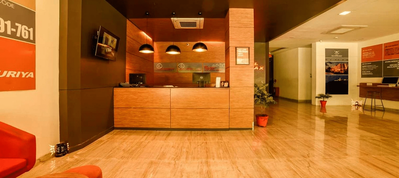 A lobby area of Max Hotel Jabalpur, featuring a wooden reception desk, a polished floor, and seating areas.