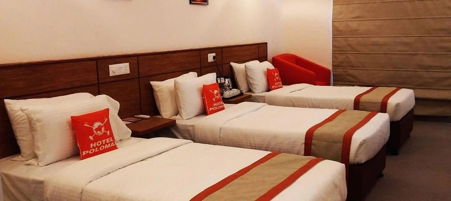 A room featuring three single beds with white linens and brown and red accents at Max Hotel Jabalpur.