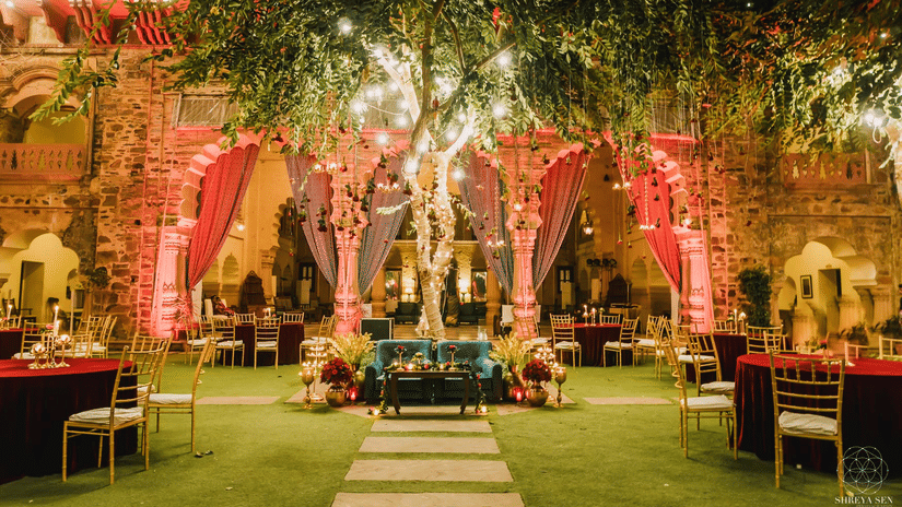 A courtyard at Tijara Fort-Palace - 19th Century, Alwar, with a central tree, decorated arches, seating, and tables set for an event.