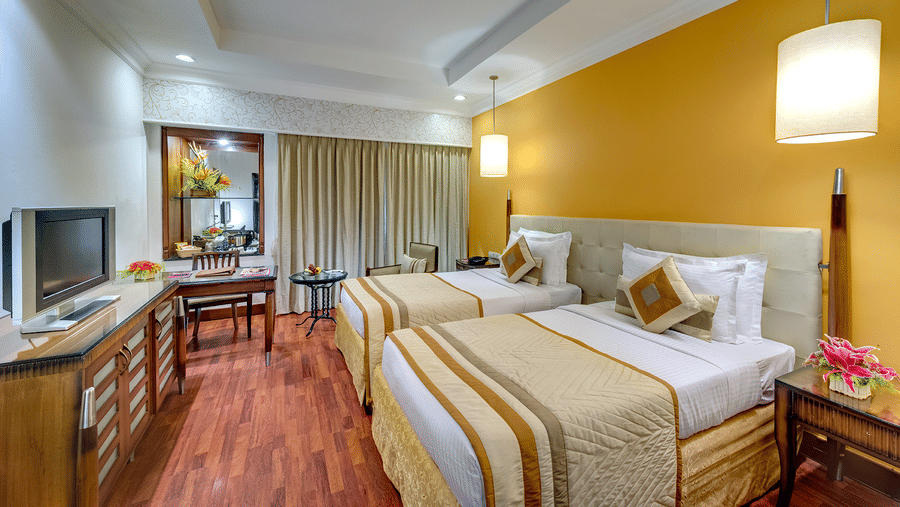 A well lit twin bed hotel room with stylish decor, wooden flooring and elegant furnishings, offering a cosy and sophisticated atmosphere – Hotel Hindusthan International, Kolkata