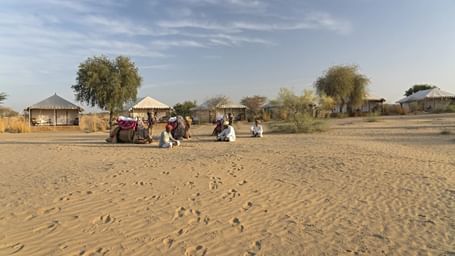 A panoramic view of a luxurious safari tent camp in the desert, with a group of people relaxing outside.