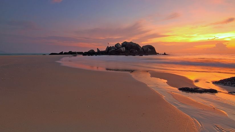 A wide view of a seashore with hues of sunset in the background