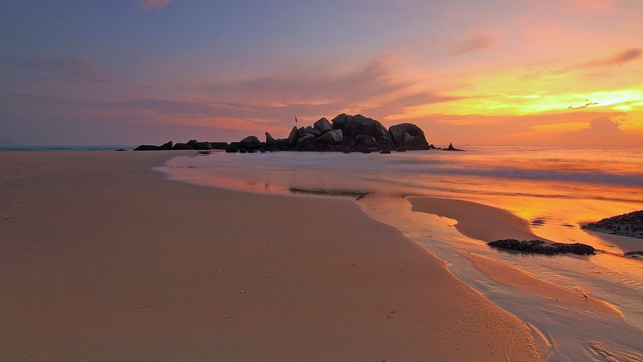 A wide view of a seashore with hues of sunset in the background