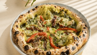 a fully loaded pizza on a white plate, with fresh basil leaves in the background at Gemini Continental