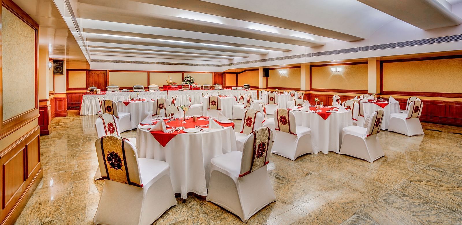 A spacious banquet hall with set tables and red chairs at Tara, Comfort Hotel in Hyderabad - Ramoji Film City.
