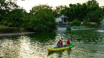 Two people paddling a yellow kayak in a calm lake surrounded by trees.
