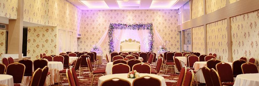 An image of a banquet hall with many table and chairs and at the front there is a stage set up, decorated with flowers and curtains 