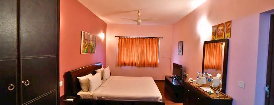 Well-furnished bedroom with a double bed, wardrobes and ambient lighting at Vedic Village Spa Resort.