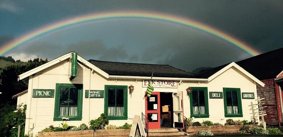 A charming white house with green shutters under a double rainbow in the sky.