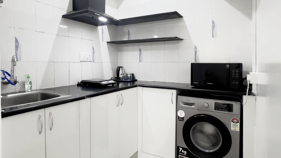 A modern kitchen in the Premium One Bedroom Apartment at The Pinnacle featuring tiled walls, a dark counter top with a built-in sink, and electronic appliances.