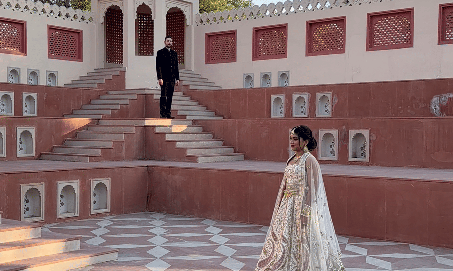 A bride walks across a geometric patterned, tessellated courtyard with red-stone stairs rising in the background at Umaid Palace.