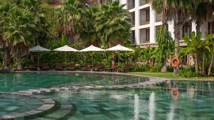 An image of a pool with several palm trees surrounded - Alibu Resort Nha Thrang