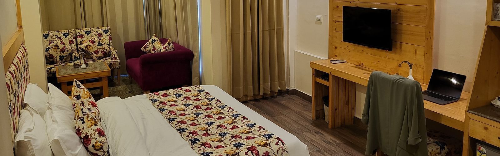 A well-lit hotel room with a bed, colourful cushions, a TV, and a work desk at Dagshai Manor Kasauli - Inde Hotels.