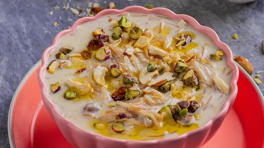 Bowl of Indian sweet dish garnished with dry fruits, set next to a small bowl of nuts.