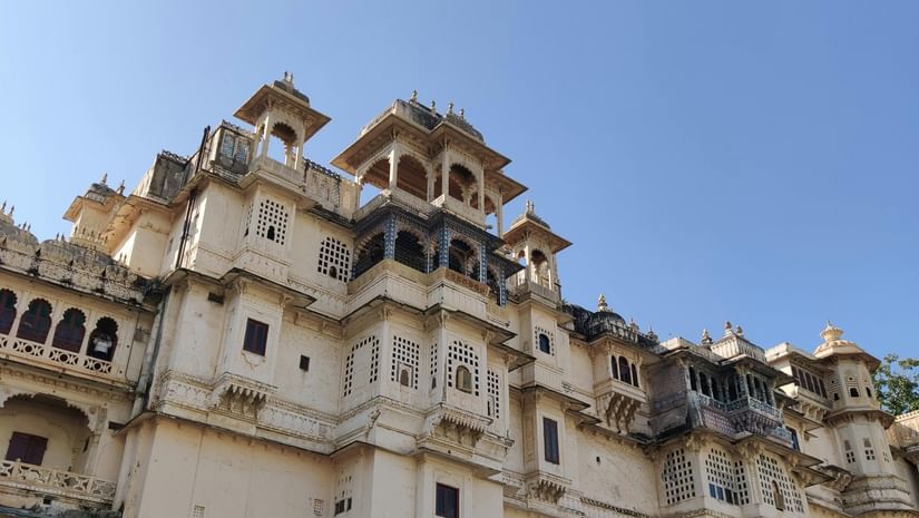 Low-angle shot of a palace, featuring its facade with multiple levels, balconies, and decorative elements under a clear blue sky.