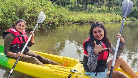 Two women in life jackets smiling while kayaking on a serene river with dense foliage in the background - Evergreen County