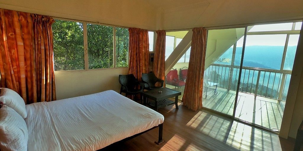 A spacious room with a large bed, a wooden table and chair in the corner, and a large balcony offering a view of nature at Wind Chalet Resort.