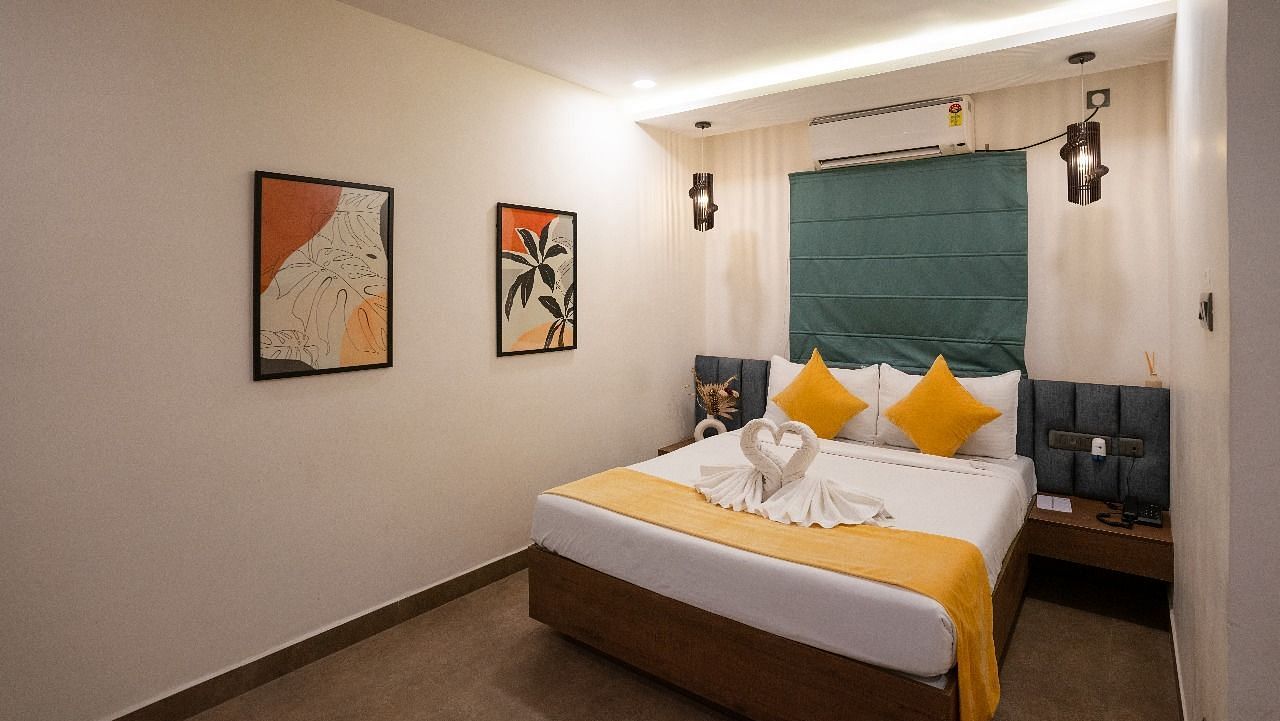 A side view of the room showcasing the bed, warm lighting, wall decor, and a large window offering natural light at Hotel Kyzen Smartstays – Smart, Reliable, Kyzen