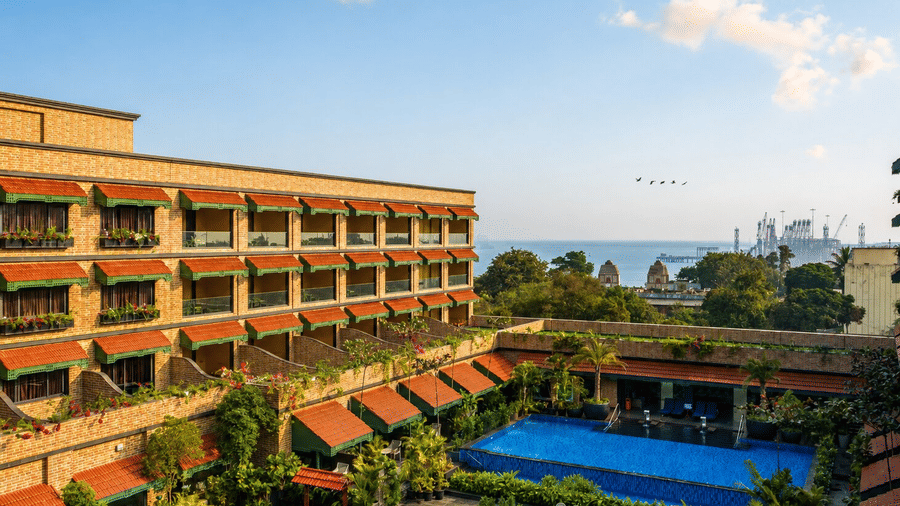 An outdoor swimming pool surrounded by brick buildings overlooking the nearby coast at MAYFAIR Bay Resort, Paradeep.