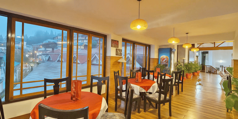 Orchid Restaurant at Central Heritage Resort and Spa, Darjeeling featuring several sets of table and chairs, plants across the dining space, and windows which provides outside view