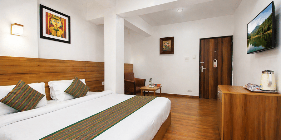 Interior view of the Annex Deluxe room at Central Hotels featuring a king bed with striped runner wooden headboard hardwood flooring framed artwork wall-mounted TV and a wooden wardrobe near the door.