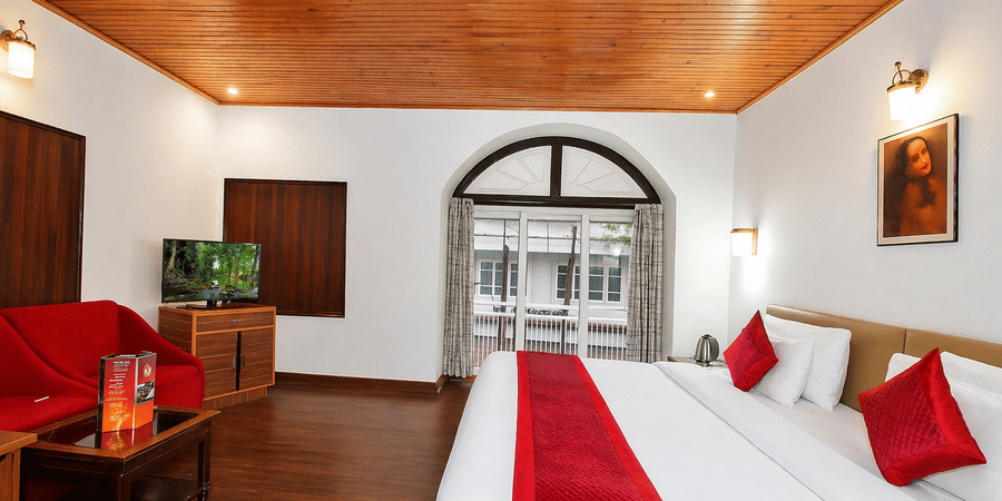 A room at Central Hotels featuring two beds with red bedding wooden ceiling a wall-mounted TV and large arched windows with a balcony view and warm ambient lighting.