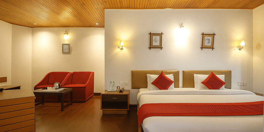 A triple bed room at Central Hotels featuring three beds with red and white bedding wooden ceiling warm wall lighting a sofa in the corner and dark hardwood flooring.