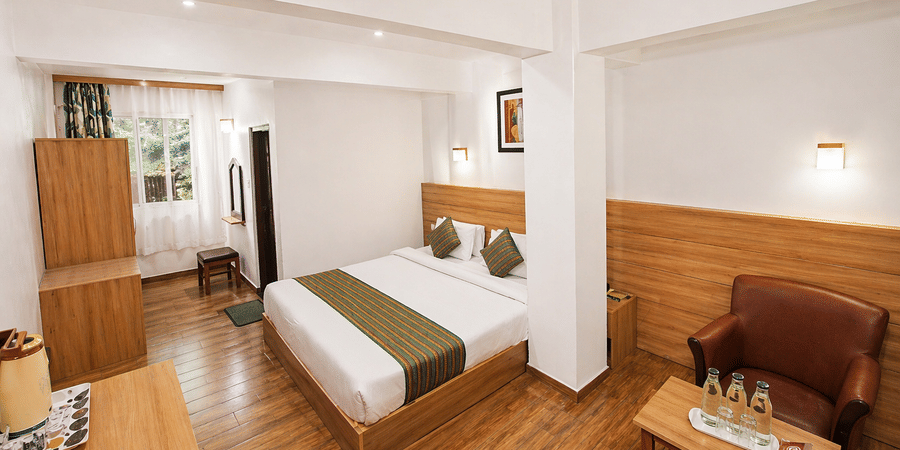 A twin bed room at Central Hotels featuring two single beds with white bedding wooden wall panels hardwood flooring a wooden wardrobe and a small seating area near the window.