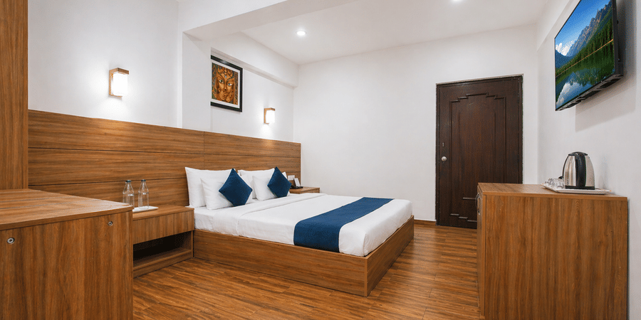 Wide angle view of a room at Central Hotels showing a king bed with blue accents wooden wall panels hardwood flooring framed artwork and a dark wooden door in the background.
