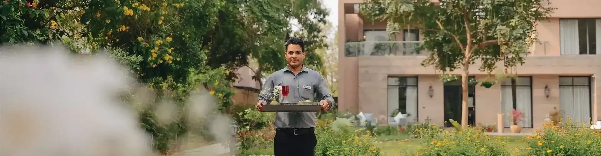 A waiter at Karma Chalets  holding a tray of food with a building behind.