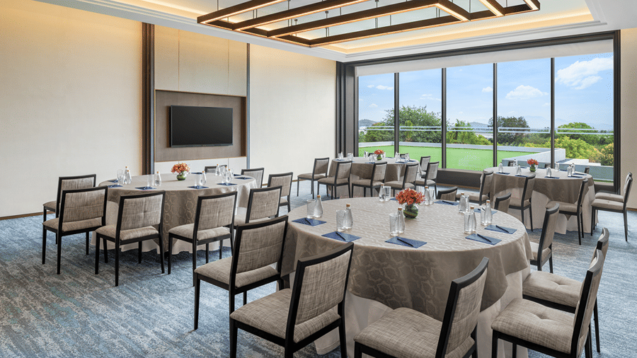 Council 1 meeting room with round tables, grey chairs, notepads, a wall-mounted screen and floor-to-ceiling windows at The Residency Signature Madurai.